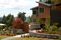 The custom home sits on a slightly sloped lot facing south. Curved concrete walls bracket the entry walk and the fence panel shields the owners from full street exposure. Plant material harmonizes with the house in the tawny brown, orange-red, and purple color scheme.